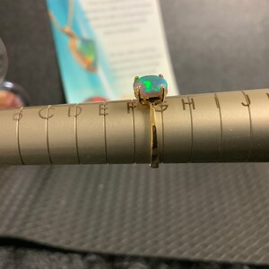 May include: A gold ring with a green and white opal gemstone. The ring is sized on a ring sizer with letters A through L.