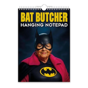 Op de afbeelding: Een hangende notitieblok met de tekst "BAT BUTCHER" in gele letters. De afbeelding toont een persoon in een zwart Batman-masker en kostuum met een geel vleermuissymbool en een roze jas.
