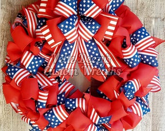 May include: A red, white, and blue patriotic wreath made with ribbon featuring the American flag. The wreath is decorated with multiple bows and is perfect for celebrating Independence Day.