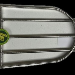 May include: A metal grill with a rounded top and three tines. The grill has a chain on the left side and a green and yellow sticker that reads "ORUNMILA LADE BOTANICA LLC".