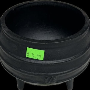 May include: A black cast iron pot with three legs and a price tag of $14.00. The pot has a rounded bottom and a wide opening.