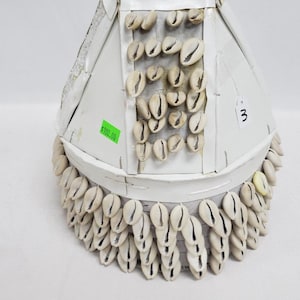 May include: White conical hat with a beaded top and a white shell design. The hat has a price tag of $100.00 and a number 3 tag.