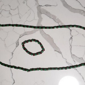 May include: A black and green beaded necklace and bracelet set. The necklace is longer and the bracelet is shorter. Both are made of small, rectangular beads.
