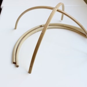 May include: Three unfinished wooden hoops, each with a slight curve, are arranged in a stack on a white surface. The hoops are made of natural wood and have a smooth finish.