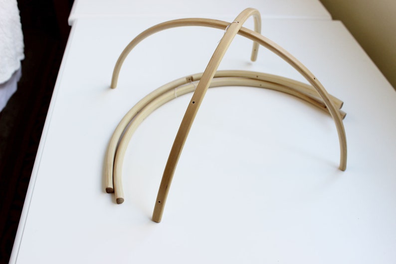 May include: Three unfinished wooden hoops, each with a slight curve, are arranged in a stack on a white surface. The hoops are made of natural wood and have a smooth finish.