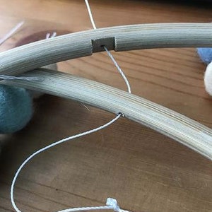 May include: A close-up of a wooden hoop with a white string threaded through a hole. The string is tied in a knot at the bottom of the hoop.