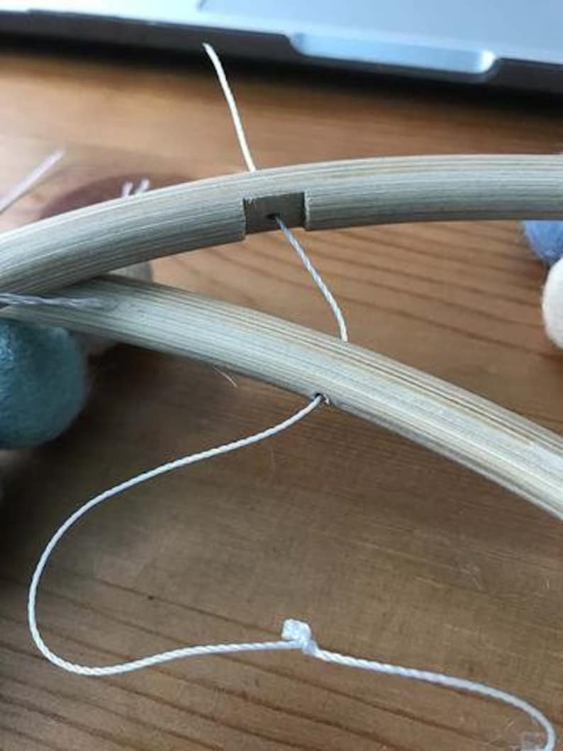 May include: A close-up of a wooden hoop with a white string threaded through a hole. The string is tied in a knot at the bottom of the hoop.