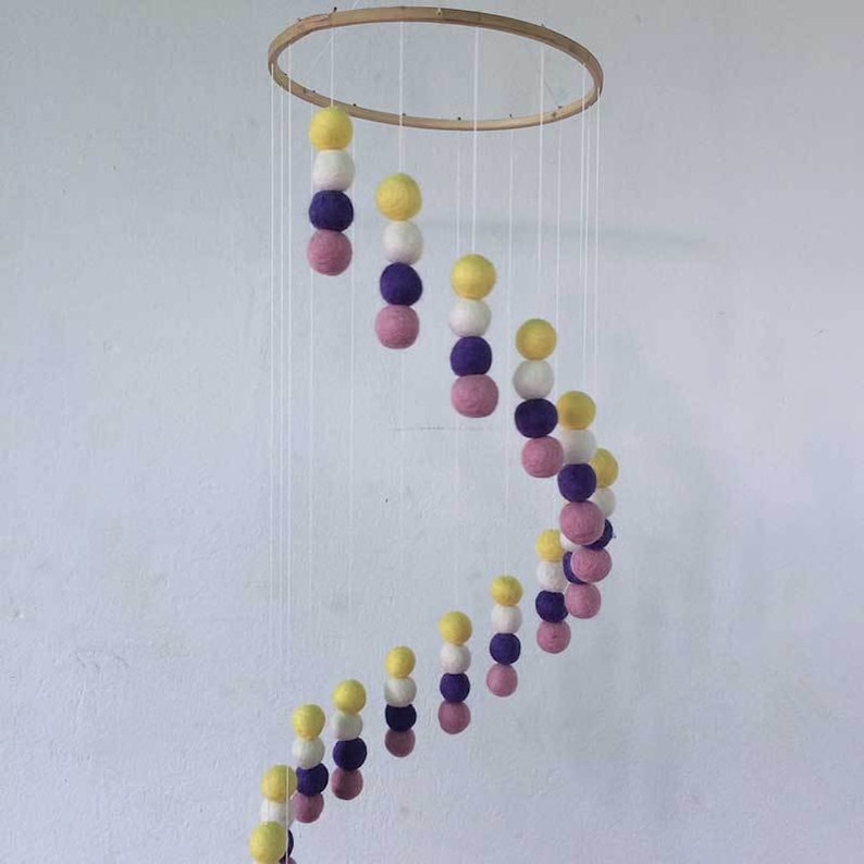 May include: A wooden hoop mobile with a spiral of felt balls in yellow, white, purple, and pink.
