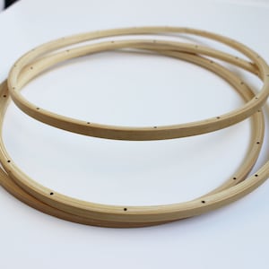 May include: Three wooden embroidery hoops of different sizes, stacked on top of each other. The hoops are made of natural wood and have small holes around the edges.