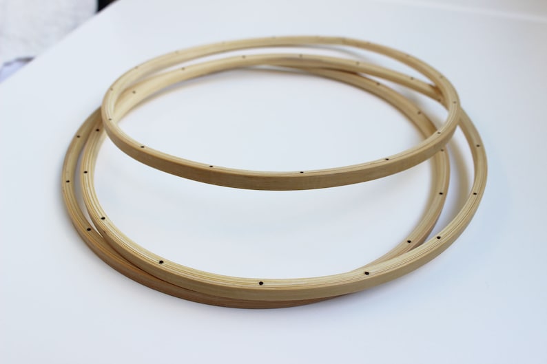May include: Three wooden embroidery hoops of different sizes, stacked on top of each other. The hoops are made of natural wood and have small holes around the edges.