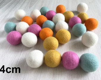 Könnte beinhalten: Eine Sammlung von 25 bunten Filzkugeln in verschiedenen Farbtönen von Rosa, Blau, Gelb, Orange und Weiß. Die Kugeln haben einen Durchmesser von 4 cm und sind in einem zufälligen Muster auf einer hellbraunen Holzoberfläche angeordnet.