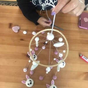 May include: A wooden baby mobile with white felt bunnies, pink felt balls, and white felt balls hanging from a wooden ring.