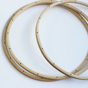 May include: Two wooden embroidery hoops, one larger than the other, are stacked on top of each other. Both hoops have small holes evenly spaced around the circumference.