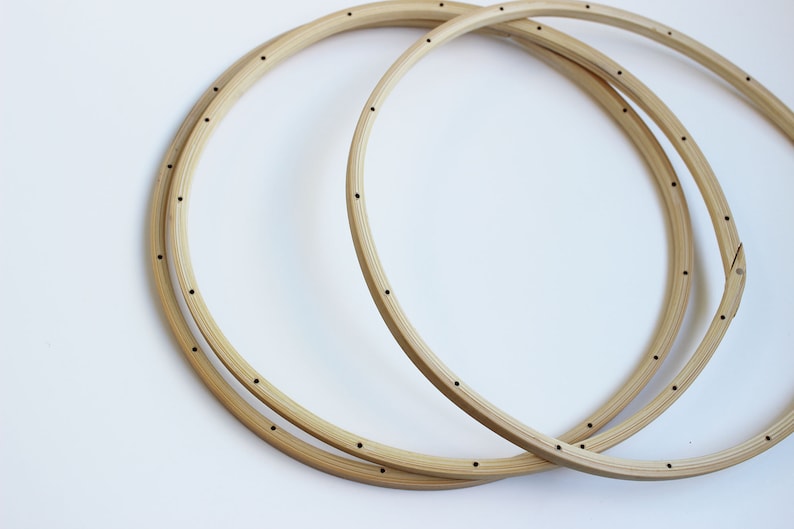 May include: Two wooden embroidery hoops, one larger than the other, are stacked on top of each other. Both hoops have small holes evenly spaced around the circumference.