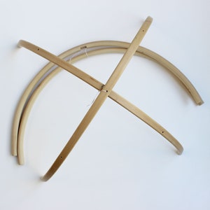 May include: A wooden mobile frame made of four curved pieces of wood that intersect in the center. The frame is designed to hold a mobile.