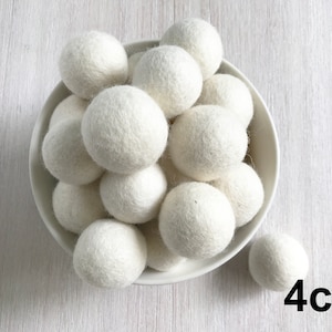May include: A white bowl filled with 14 white wool dryer balls, each measuring 4 inches in diameter. A single white wool dryer ball sits on a white surface below the bowl. 4cm