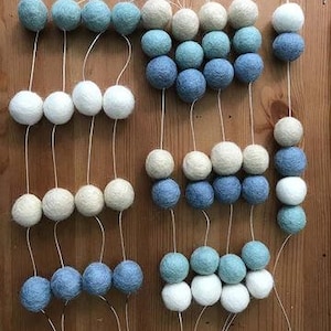 May include: A garland of white, light blue, and dark blue felt balls strung on white thread. The garland is made up of multiple strands of balls, each strand with a different color pattern.