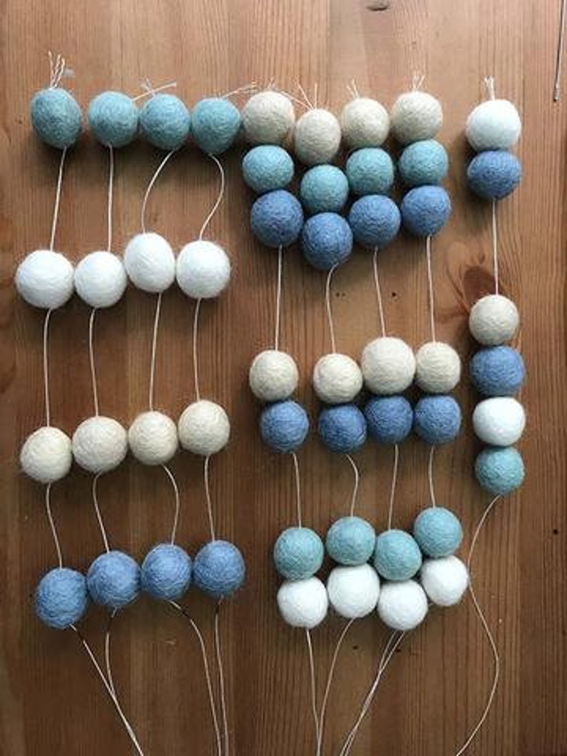 May include: A garland of white, light blue, and dark blue felt balls strung on white thread. The garland is made up of multiple strands of balls, each strand with a different color pattern.