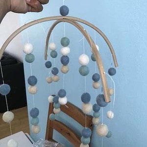 May include: A wooden baby mobile with white, blue, and green felt balls hanging from the frame. The mobile is suspended from the ceiling.