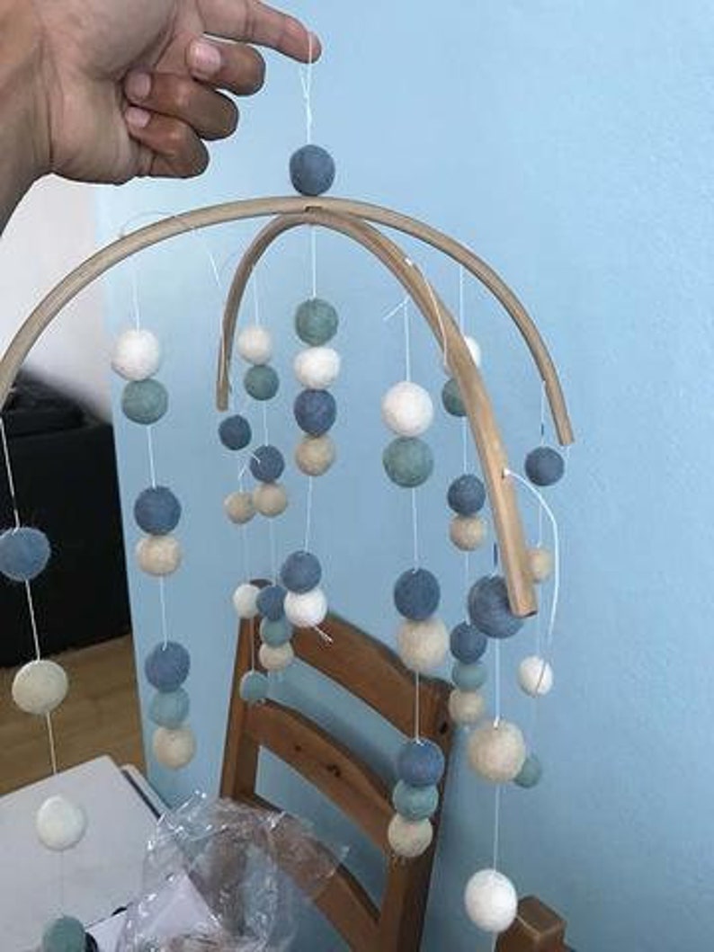 May include: A wooden baby mobile with white, blue, and green felt balls hanging from the frame. The mobile is suspended from the ceiling.