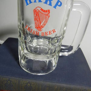 May include: Clear glass beer mug with a handle. The mug features the word "HARP" in blue, above a red and white harp graphic, and the words "IRISH BEER" in red.
