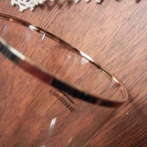 May include: A clear glass with a gold rim and the word "WARSTEINER" printed on the side. The glass is set against a brown wooden surface.