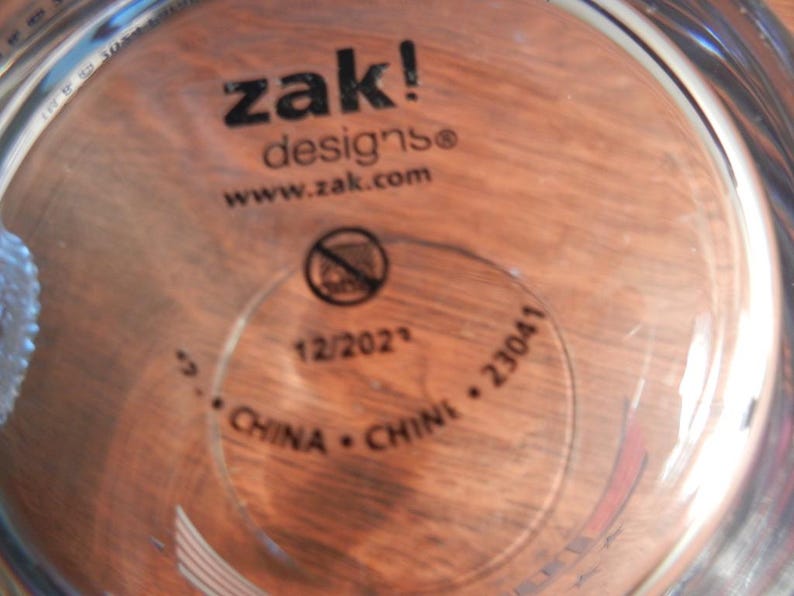 May include: Clear glass cup with the text "zak! designs" and "www.zak.com" printed in black. The bottom of the cup has a circular stamp with the text "12/2021", "CHINA", and "23041".
