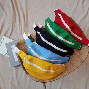 K&ouml;nnte beinhalten: F&uuml;nf Bauchtaschen in verschiedenen Farben: Gelb, Blau, Schwarz, Gr&uuml;n und Rot. Jede Bauchtasche hat einen wei&szlig;en Rei&szlig;verschluss.