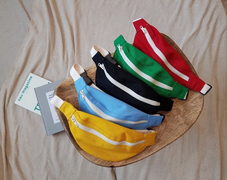 K&ouml;nnte beinhalten: F&uuml;nf Bauchtaschen in verschiedenen Farben: Gelb, Blau, Schwarz, Gr&uuml;n und Rot. Jede Bauchtasche hat einen wei&szlig;en Rei&szlig;verschluss.