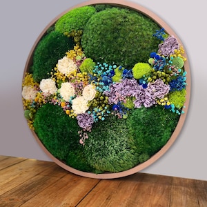 May include: A round, framed wall art piece featuring preserved moss and dried flowers in shades of green, white, yellow, blue, and purple.