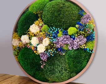 May include: A round, framed wall art piece featuring preserved moss and dried flowers in shades of green, white, yellow, blue, and purple.