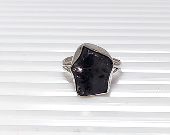 May include: A silver ring with a large, black, rough-cut gemstone. The ring is set in a simple band.