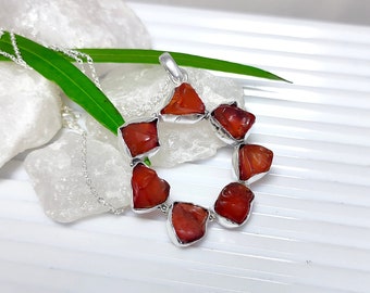 May include: A silver necklace with a pendant made of seven red carnelian stones set in silver. The stones are arranged in a circle.