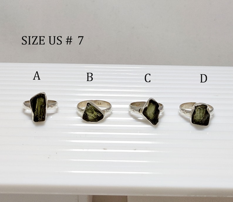 Pu&ograve; includere: Quattro anelli d'argento con pietre preziose verdi. Gli anelli sono etichettati con le lettere A, B, C e D. Il testo "SIZE US # 7" &egrave; nella parte superiore dell'immagine.