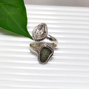 Puede incluir: Un anillo de plata con dos piedras preciosas en bruto. El anillo es de diseño retorcido con una piedra clara y una piedra verde.