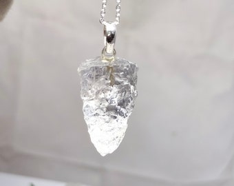 May include: A clear quartz crystal pendant on a silver chain. The crystal is faceted and has a rough, natural look.