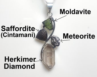 May include: A silver pendant necklace with four different stones: a green moldavite, a black meteorite, a gray herkimer diamond, and a black safflordite (cintammani).