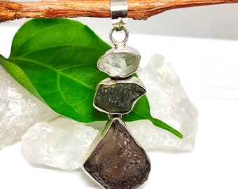 May include: A silver pendant featuring three stacked, raw, natural gemstones. The top stone is clear quartz, the middle stone is green, and the bottom stone is brown.