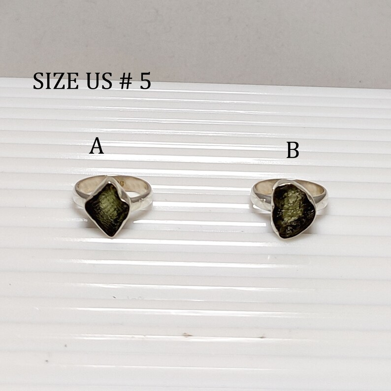 Pu&ograve; includere: Due anelli d'argento con pietre preziose verdi. Gli anelli sono etichettati A e B. Il testo "SIZE US # 5" &egrave; in alto nell'immagine.