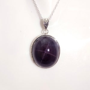 May include: A silver chain necklace with a pendant featuring a dark purple star-shaped gemstone set in a silver oval frame.