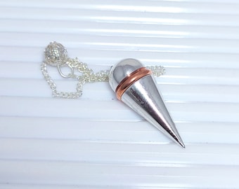 Op de afbeelding: Een zilveren en koperen slinger met een ketting. De slinger is kegelvormig en heeft een koperen band rond de bovenkant.