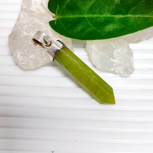 Könnte beinhalten: Ein grüner Edelstein-Anhänger mit einer silbernen Öse. Der Anhänger ist in Form einer langen, dünnen Spitze geformt.