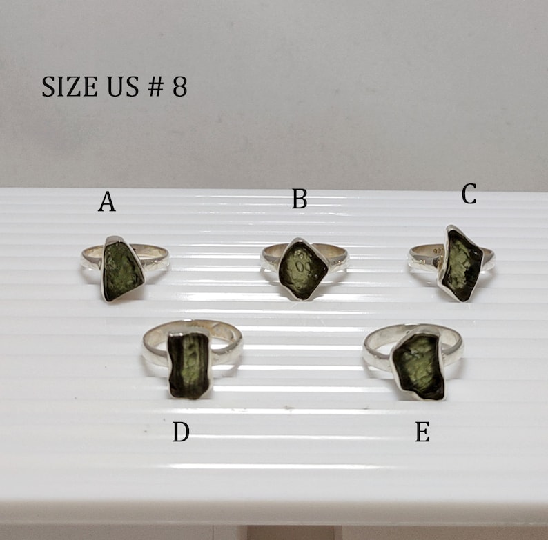 Pu&ograve; includere: Cinque anelli d'argento con pietre preziose verdi. Gli anelli sono etichettati con le lettere A, B, C, D ed E. Il testo "SIZE US # 8" &egrave; nella parte superiore dell'immagine.