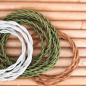 May include: Close-up of three spools of twisted fabric-covered electrical wire. The spools are in white, olive green, and brown. The wires are arranged on a bamboo surface.