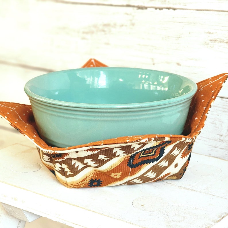 Peut inclure: Un bol en c&eacute;ramique bleu-vert est plac&eacute; dans un r&eacute;chauffeur de bol en tissu &agrave; motifs marrons et blancs. Le r&eacute;chauffeur a un motif g&eacute;om&eacute;trique avec des accents marrons, blancs et noirs.
