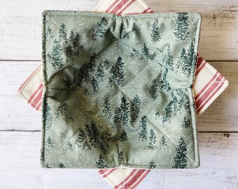 Peut inclure: Un protège-bol matelassé vert et blanc avec un motif de forêt. Le protège-bol est plié et posé sur un tissu rayé rouge et blanc.