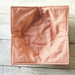 May include: A pink and white polka dot fabric bowl liner. The liner is folded and has a square shape.