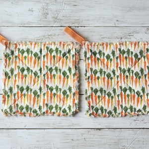 May include: Two white cotton pot holders with a carrot print. The pot holders have orange and green carrots on a white background. The pot holders have orange fabric ties.