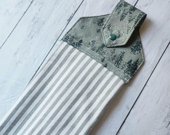 Peut inclure: Un torchon de cuisine suspendu avec un corps rayé et une section supérieure avec un motif de forêt. La section supérieure est de couleur vert clair avec une fermeture à bouton. Le corps de la serviette a des rayures verticales blanches et vert clair.