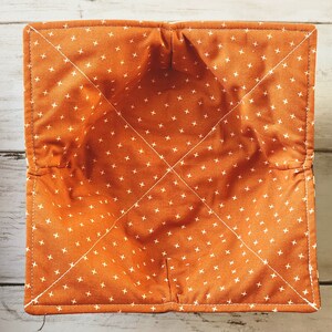 Peut inclure: Bol en tissu orange avec un motif de croix blanches. Le bol est fait d'un tissu doux et matelass&eacute; et a une forme carr&eacute;e.
